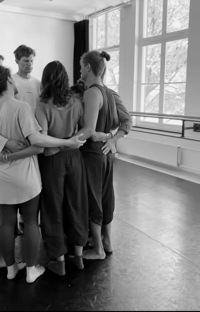 Groep staat in een kring met de armen om elkaar heen in een dansstudio